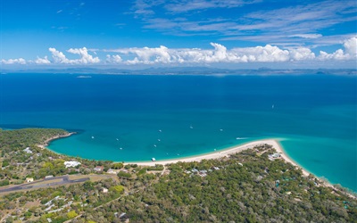 Aerial view of Great Keppel Island, with a sandy beach with anchored boats, surrounded by lush greenery and clear blue ocean.