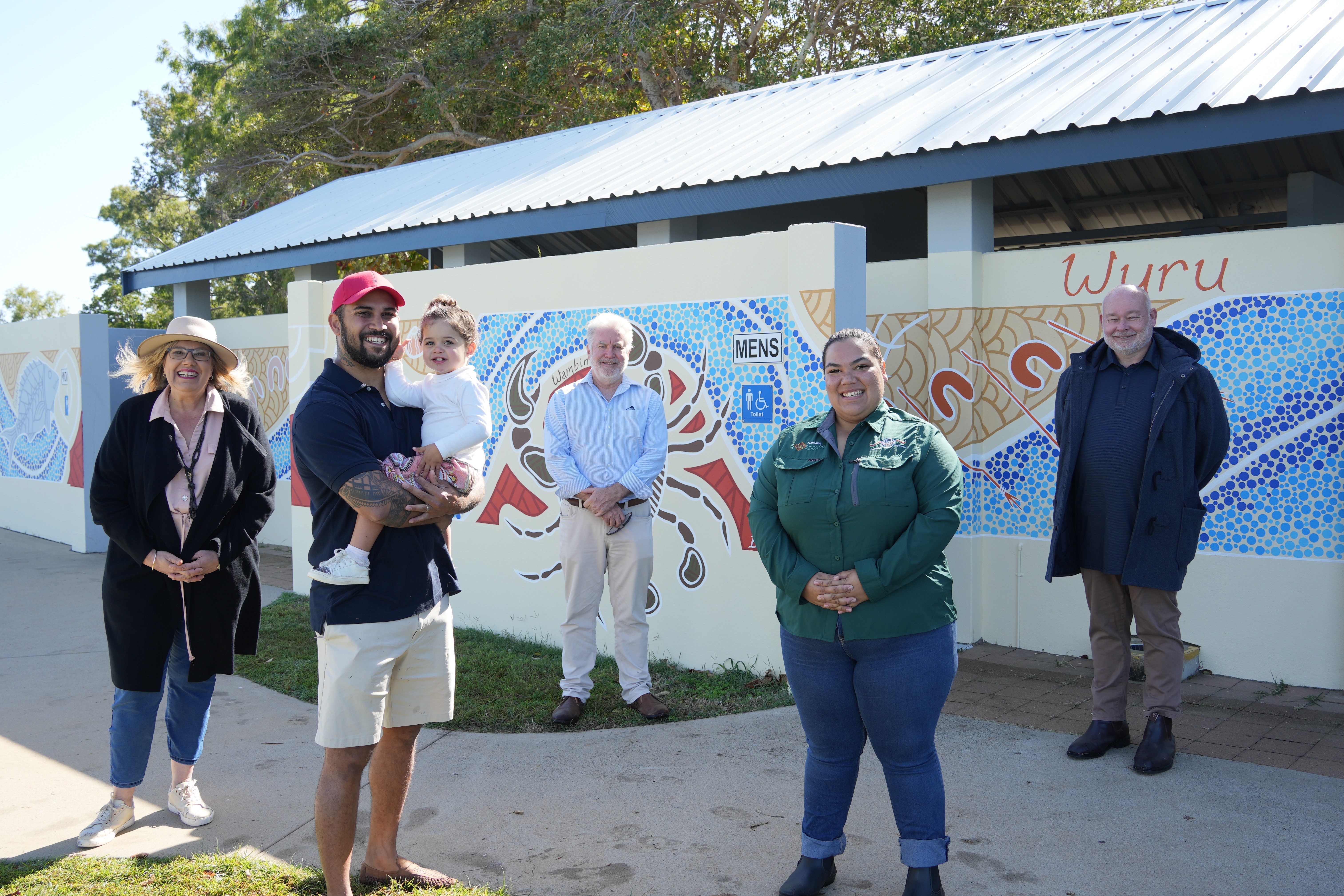 Group of six people, including a child, standing in front of a mural-covered building with an accessible toilet sign.
