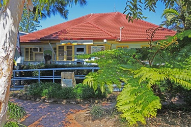 Community Centre building with a red-tiled roof and yellow window frames, surrounded by greenery and a stone plaque near the entrance.