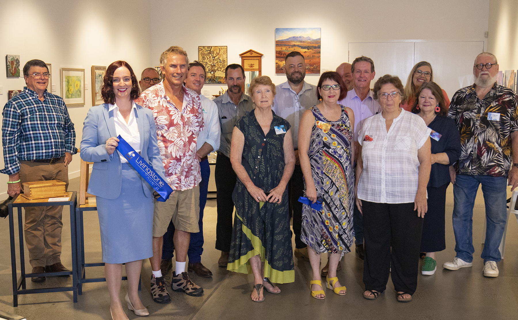 Group of people in an art gallery with one person holding a “Livingstone Beautiful” ribbon, surrounded by displayed paintings and framed artwork.