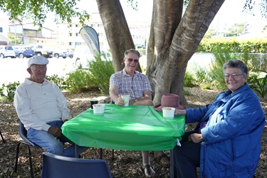 Three people sitting at an outdoor table with a green tablecloth