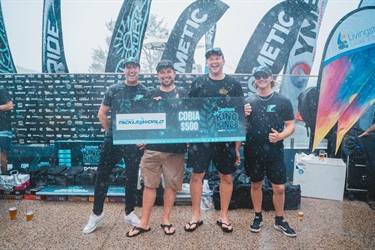 Four people holding a large cheque for $500 from The Secret Weapon Tackle World at a Capricorn King Kings event, with sponsor banners in the background.