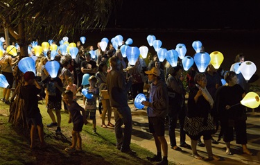 People gathered outdoors at night holding blue, yellow, and white lanterns during a lantern festival.
