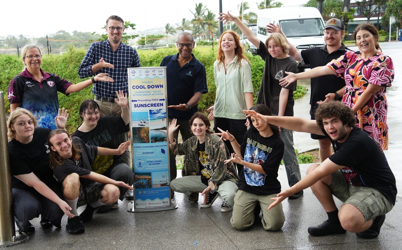 Group of people from Project Cool Down standing around a sign promoting free sunscreen, with application instructions and supporting organisations listed.